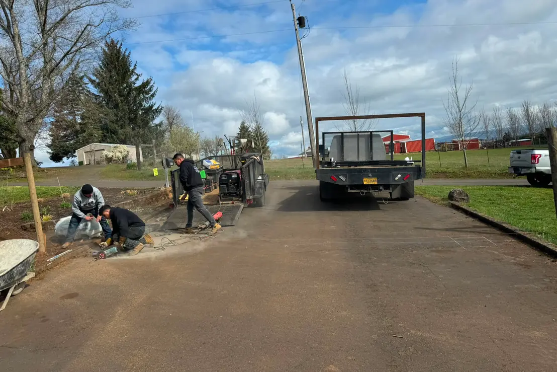 Crew cutting pipe by flatbed truck and equipment trailer on rural driveway