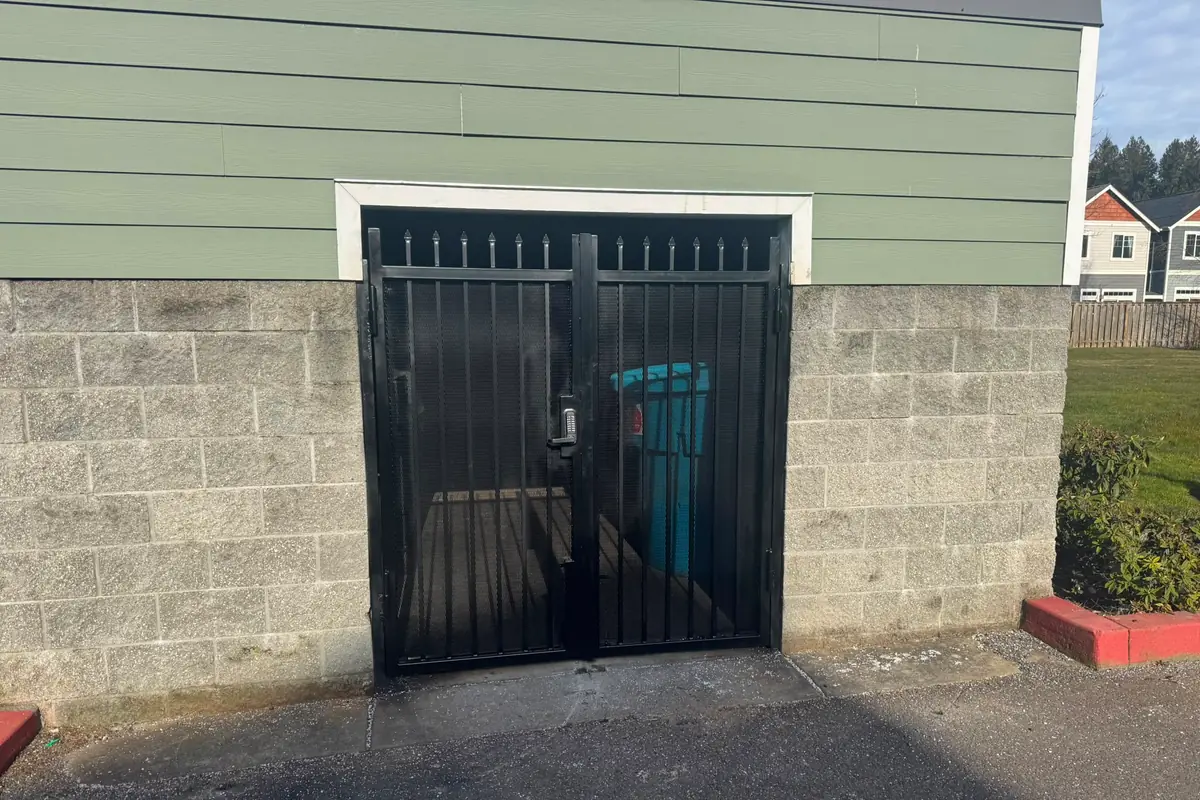 Double black metal mesh security gate with keypad on cinder-block trash enclosure
