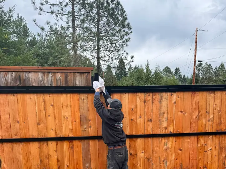 Installer reaching top rail of cedar sliding gate during construction