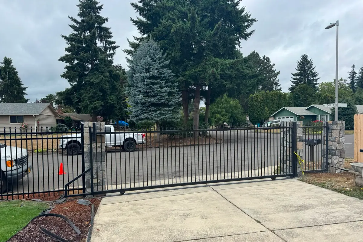 Black iron cantilever slide gate closed across driveway with stone columns, cloudy day