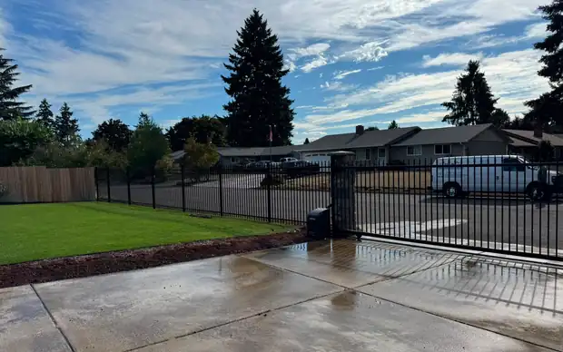 Black iron slide gate with operator and ornamental fence enclosing lawn, van across street — Interstate Gate Repair