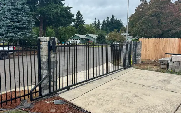 Black ornamental iron slide gate with stone columns across residential driveway — Interstate Gate Repair