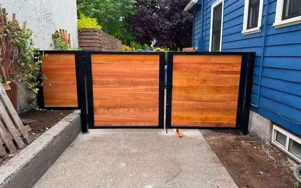 Horizontal cedar double swing driveway gate in black steel frame between houses — Interstate Gate Repair