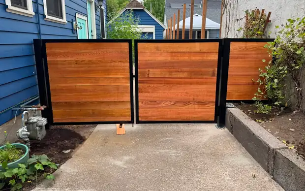 Horizontal cedar swing gate in steel frame viewed from driveway between blue and stucco houses — Interstate Gate Repair