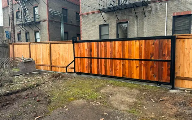 Vertical cedar cantilever slide gate in black steel frame beside cedar fence, urban lot — Interstate Gate Repair