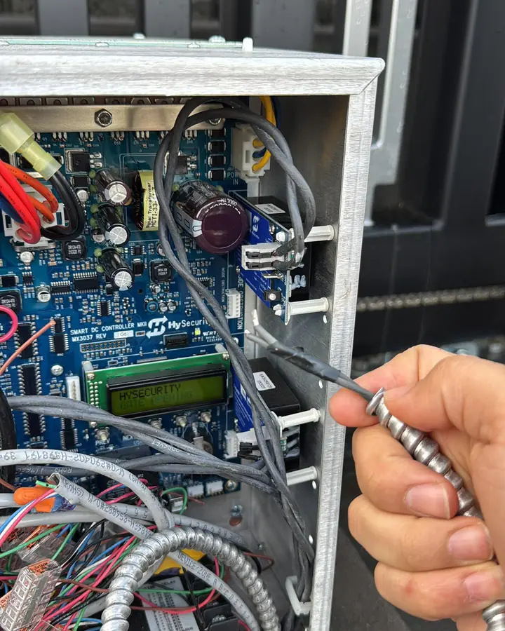 Technician probing HySecurity Smart DC controller MKII inside gate operator cabinet — Interstate Gate Repair