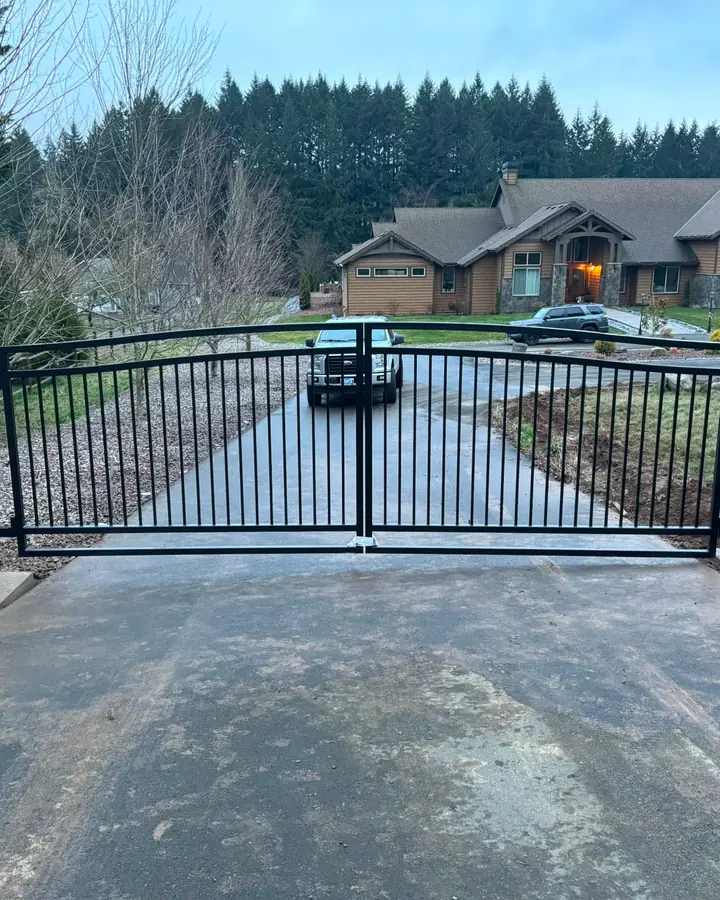 Finished black arched double swing driveway gate closed, large home and flag behind — Interstate Gate Repair