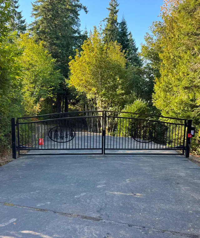 Black ornamental iron double swing driveway gate with tree design, wooded rural driveway — Interstate Gate Repair