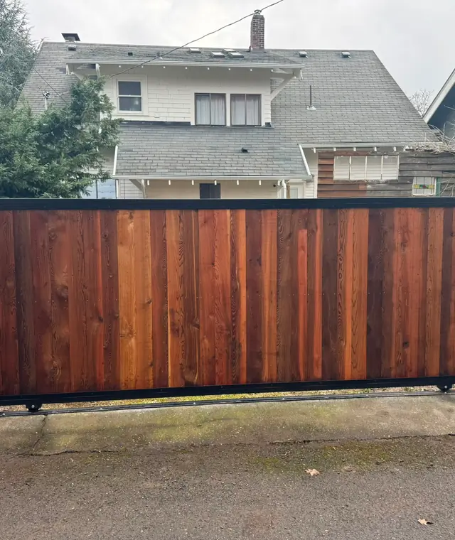 Finished cedar-clad rolling slide gate with black steel frame between wood fence panels in alley — Interstate Gate Repair