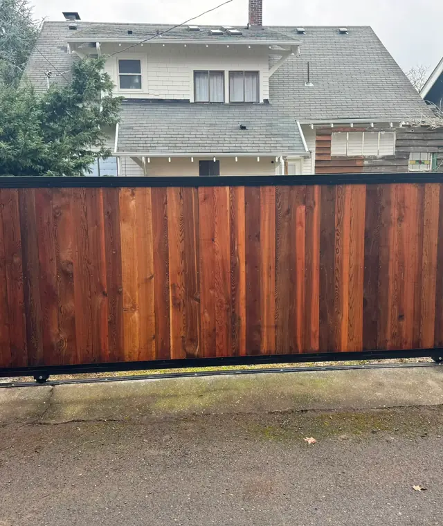 Completed cedar slide gate with steel frame on residential alley, houses behind — Interstate Gate Repair