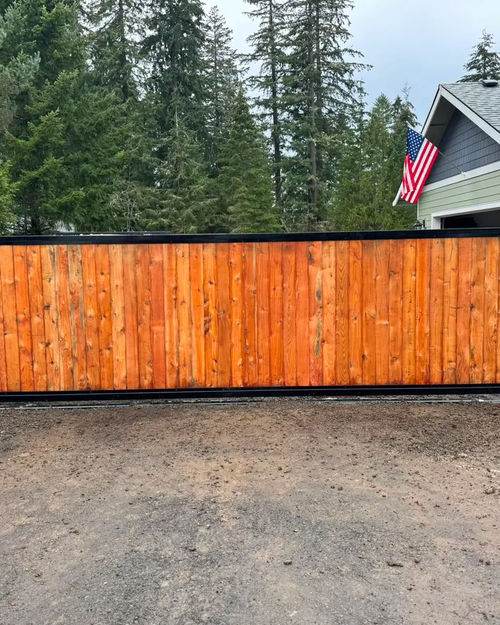 Finished cedar-infill black-steel rolling driveway gate at wooded rural home