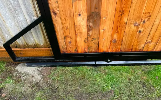 Detail of bottom corner of cedar gate showing steel frame and roller