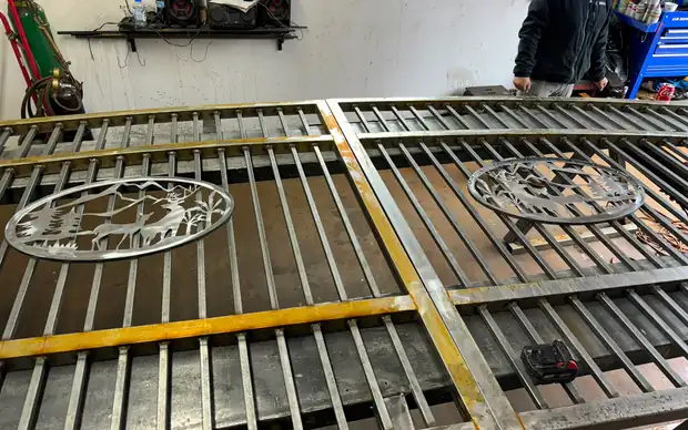 Two steel gate panels with deer scenic medallions on shop table, fabricator working