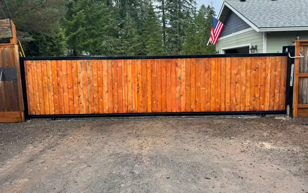 Finished cedar-infill black-steel rolling driveway gate at wooded rural home — Interstate Gate Repair