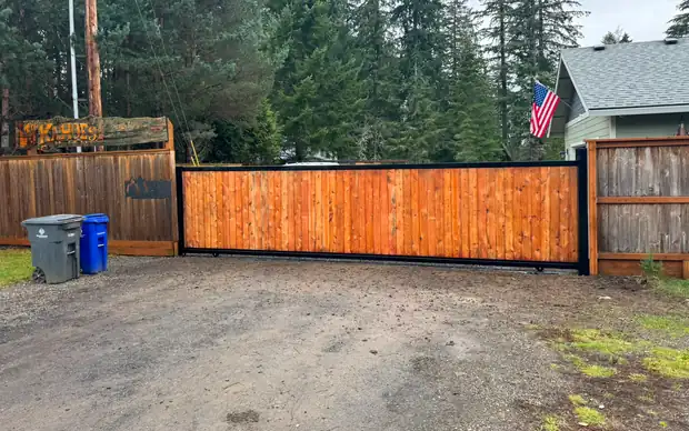 Wide view of finished cedar rolling driveway gate with property sign and flag — Interstate Gate Repair
