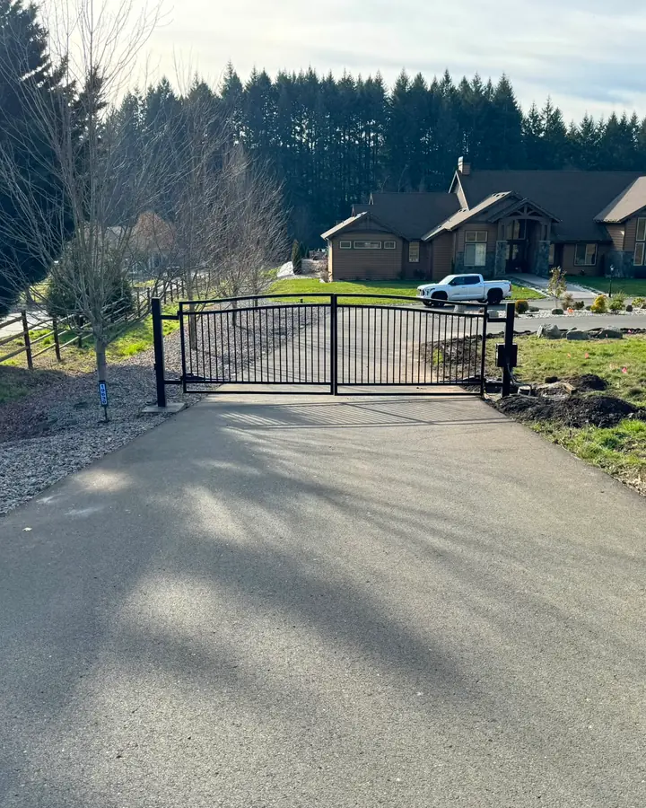 Closed arched black metal driveway gate with estate home and flag in background — Interstate Gate Repair