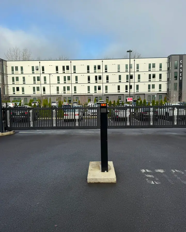 Black bi-parting slide gate closed in front of Casey apartments with bollard — Interstate Gate Repair
