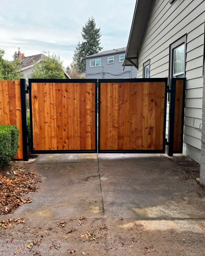 Double cedar swing driveway gate with black steel frame between houses — Interstate Gate Repair