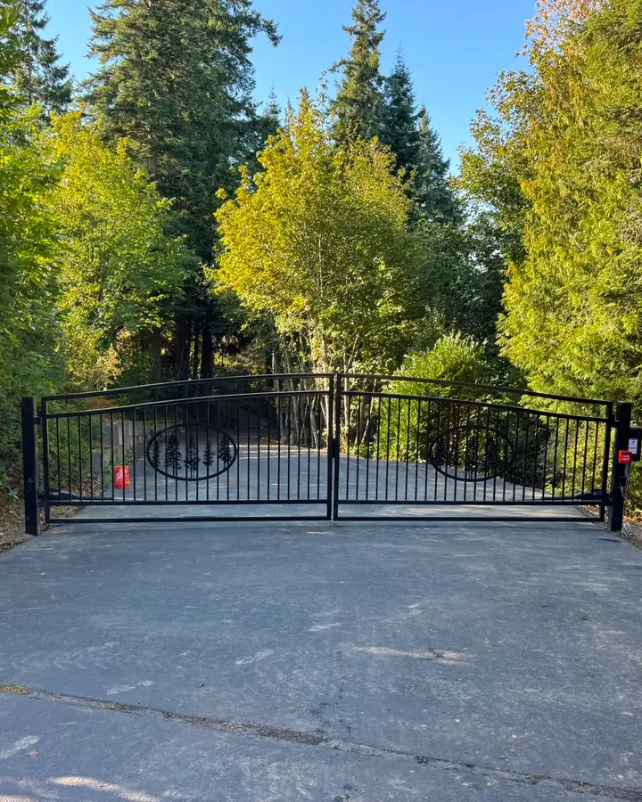 Black ornamental iron double swing driveway gate with tree design, wooded rural driveway — Interstate Gate Repair