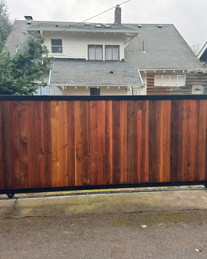 Finished cedar-clad rolling slide gate with black steel frame between wood fence panels in alley — Interstate Gate Repair