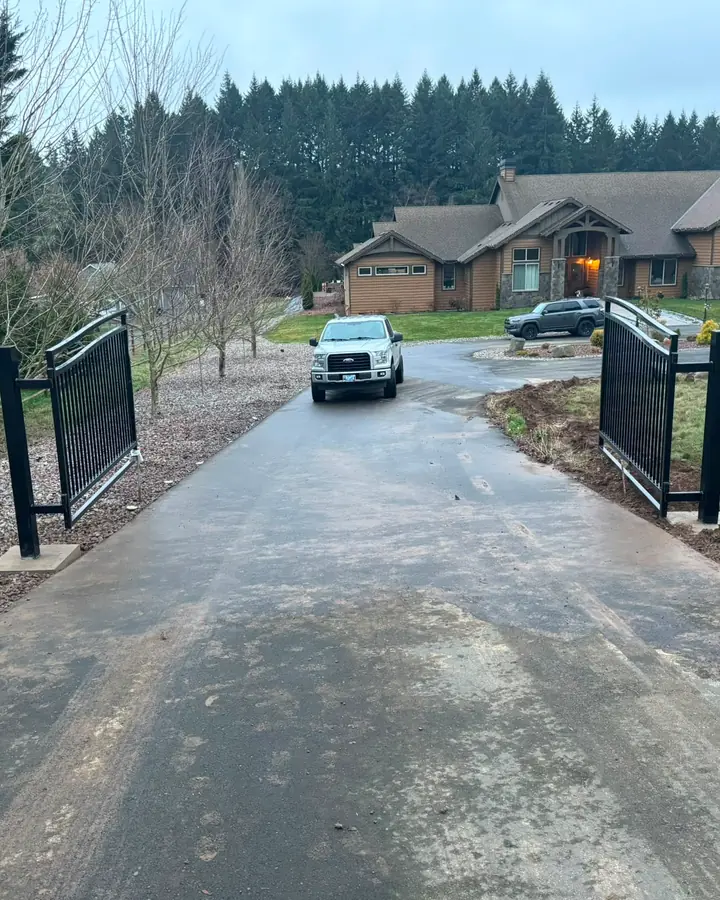 Finished black metal double swing driveway gate open, truck and large home behind — Interstate Gate Repair