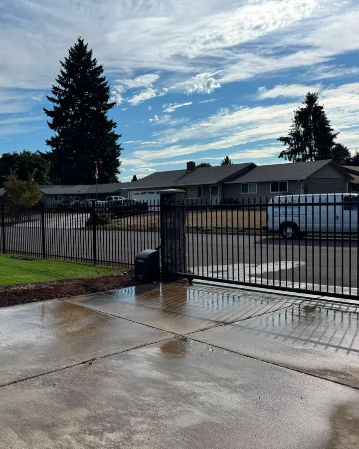 Black iron slide gate with operator and ornamental fence enclosing lawn, van across street — Interstate Gate Repair