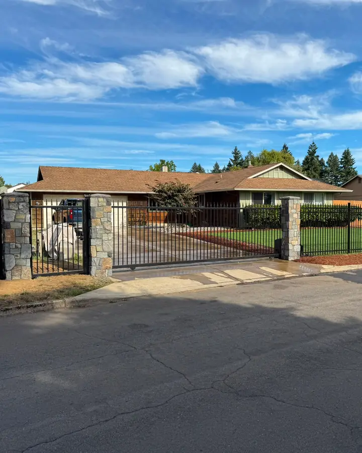 Wide view of ranch home behind black iron fence, stone columns and slide gate — Interstate Gate Repair