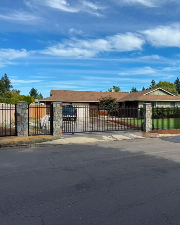 Wide view of ranch home with black iron fence, slide gate and stone columns on lawn — Interstate Gate Repair