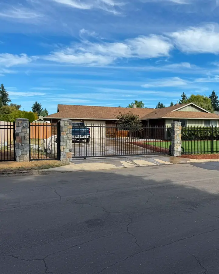 Street view of ranch house behind ornamental iron fence with stone columns and gate — Interstate Gate Repair