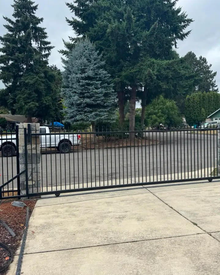 Black iron cantilever slide gate closed across driveway with stone columns, cloudy day — Interstate Gate Repair