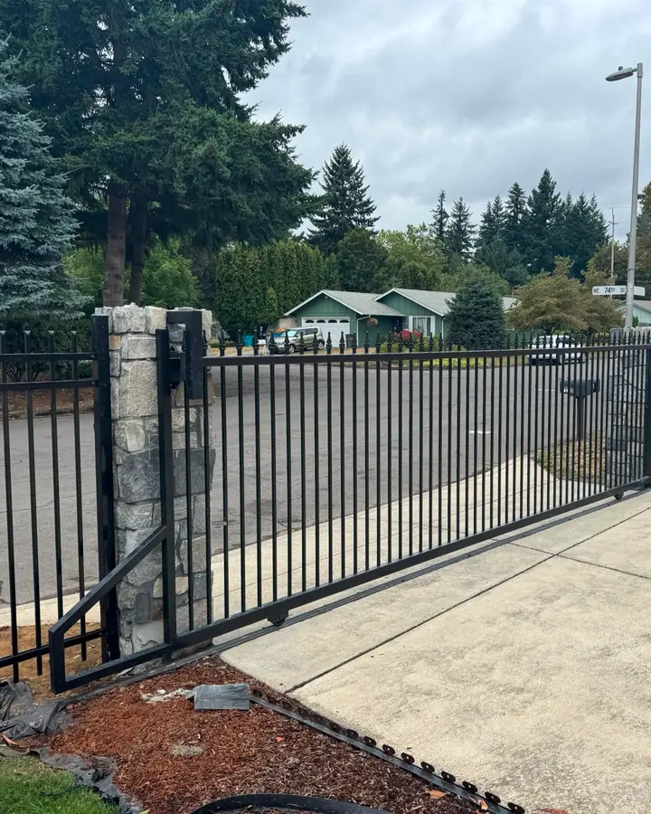 Black ornamental iron slide gate with stone columns across residential driveway — Interstate Gate Repair