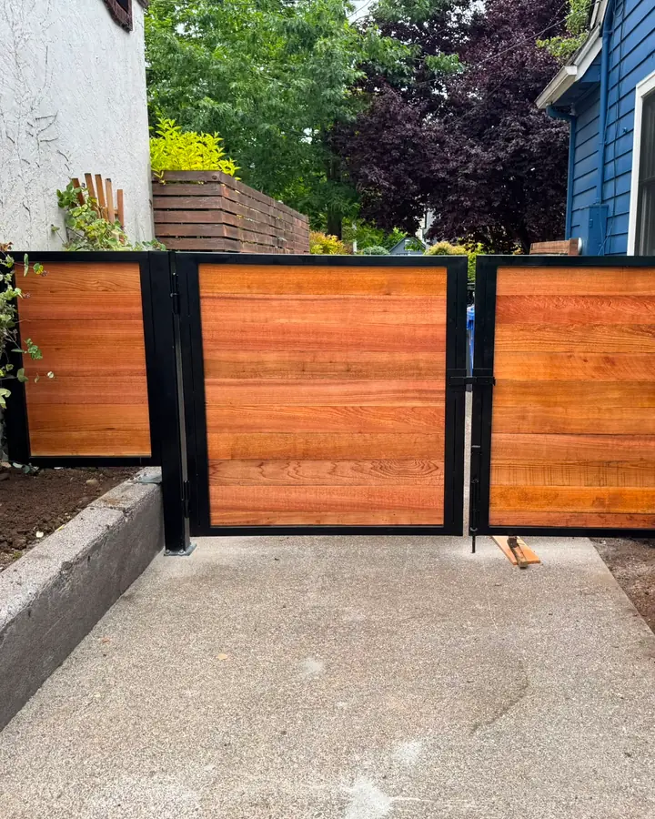 Horizontal cedar double swing driveway gate in black steel frame between houses — Interstate Gate Repair