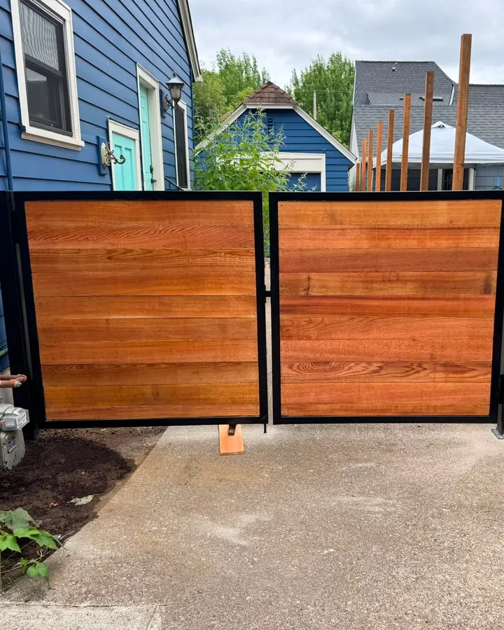 Horizontal cedar swing gate in steel frame viewed from driveway between blue and stucco houses — Interstate Gate Repair