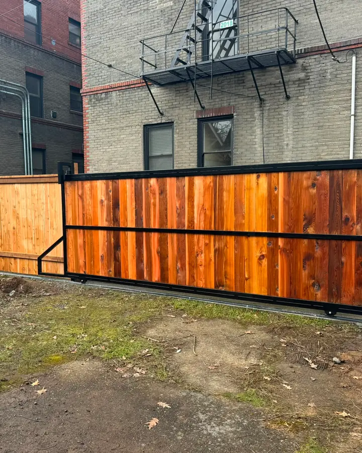 Vertical cedar cantilever slide gate in black steel frame beside cedar fence, urban lot — Interstate Gate Repair