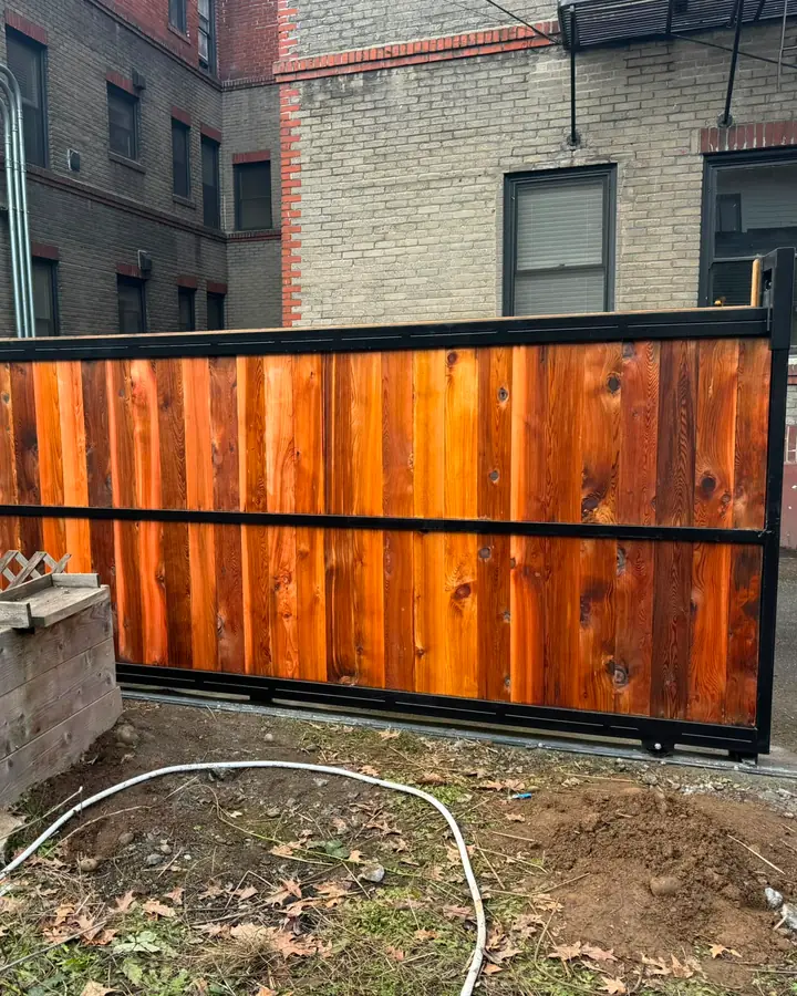 Cedar cantilever slide gate in black frame beside brick apartments and cedar fence — Interstate Gate Repair