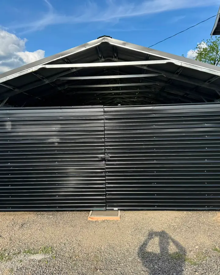 Black metal double swing gate on open-topped steel carport, sunny — Interstate Gate Repair