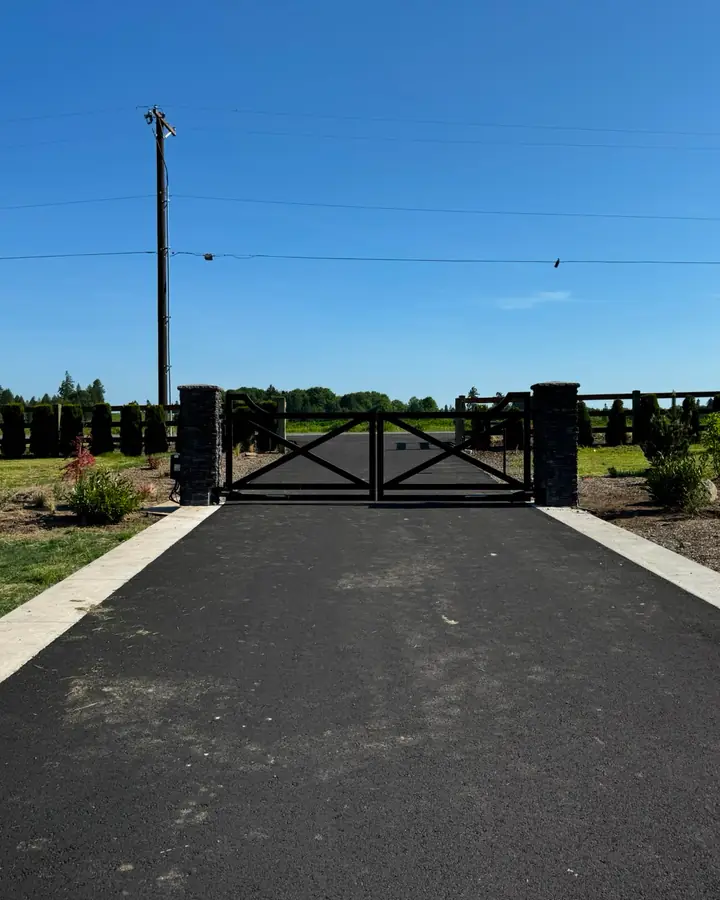 Distant view of black driveway gate with stone columns along ranch fence — Interstate Gate Repair