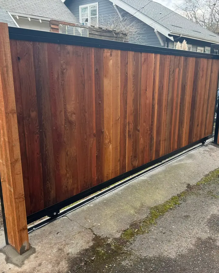 Cedar slide gate on steel track being installed on residential driveway, worker at right — Interstate Gate Repair