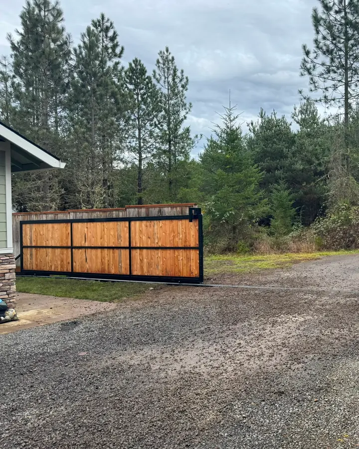 Rural driveway with open cedar rolling gate, gravel road and parked trucks — Interstate Gate Repair