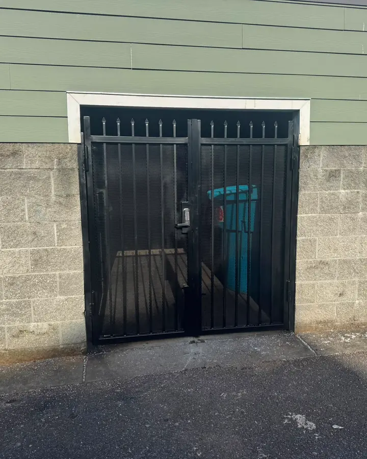 Double black metal mesh security gate with keypad on cinder-block trash enclosure — Interstate Gate Repair